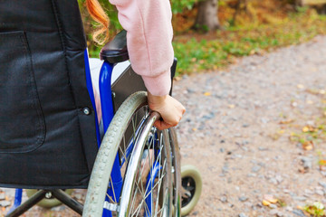Naklejka premium Hand handicap woman in wheelchair wheel on road in hospital park waiting for patient services. Unrecognizable paralyzed girl in invalid chair for disabled people outdoors. Rehabilitation concept.