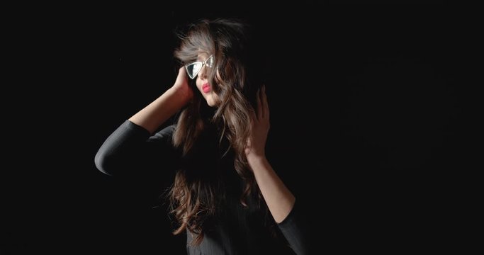 Pretty dark-haired curly woman in elegant dress and sunglasses posing to camera, glamour
