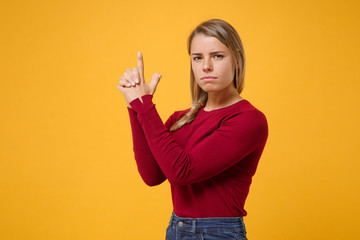 Confident young blonde woman girl in casual clothes posing isolated on yellow orange background studio portrait. People sincere emotions lifestyle concept. Mock up copy space. Holding hands like gun.