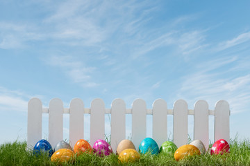 Spring grass and wooden fence with easter eggs on cloudy sky