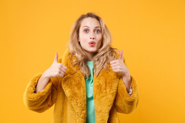 Amazed pretty young blonde woman girl in yellow fur coat posing isolated on orange wall background...