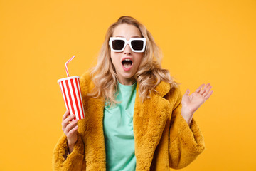 Obraz premium Zszokowany młoda blondynka kobieta dziewczyna w ciemnych okularach przeciwsłonecznych żółte futro pozowanie na białym tle na pomarańczowym tle. Koncepcja stylu życia ludzi. Makieta miejsca na kopię. Trzymaj za ręce plastikowy kubek coli lub sody.