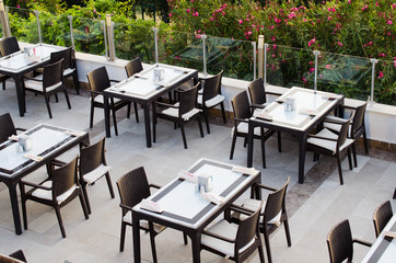 Wattled tables and chairs on terrace summer cafe overlooking the green park.
