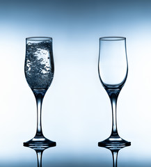Closeup photo of two glasses empty and with sparkling water on gradient white and blue background