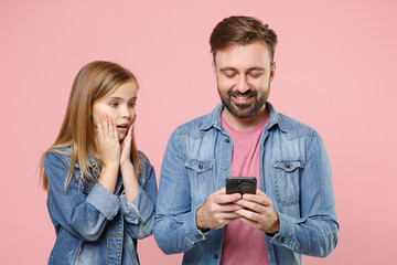 Excited bearded man in casual clothes with child baby girl. Father little kid daughter isolated on pastel pink background. Love family parenthood childhood concept Use mobile phone typing sms message.