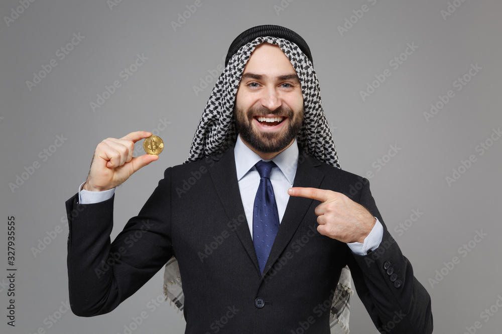 Sticker Funny arabian muslim businessman in keffiyeh kafiya ring igal agal classic suit isolated on gray background. Achievement career wealth business concept. Point index finger on bitcoin, future currency.