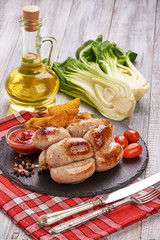 Roasted sausages, bratwurst with tomato sauce, spices and herbs on a stone plate, rustic background