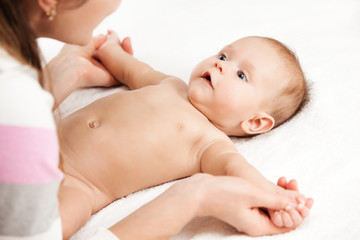 Close up of adorable infant lying on soft white sheets and looking at mommy. Young woman holding tiny hands of cute newborn child. Concept of motherhood and infancy.