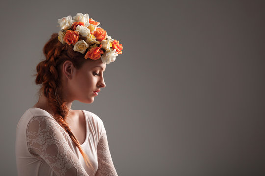 Side view of beautiful young woman with flowers on head looking down. Pretty girl wearing elegant bodysuit. Isolated on white studio background. Concept of beauty and sensuality.