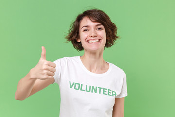 Cheerful young brunette woman in white volunteer t-shirt isolated on pastel green wall background...