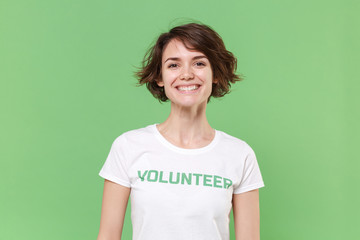 Smiling young brunette woman in white volunteer t-shirt isolated on pastel green wall background...