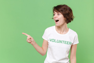 Surprised young brunette woman in white volunteer t-shirt isolated on pastel green background in...