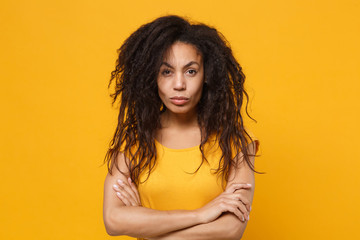 Dissatisfied young african american woman girl in casual t-shirt posing isolated on yellow orange wall background studio portrait. People lifestyle concept. Mock up copy space. Holding hands crossed.