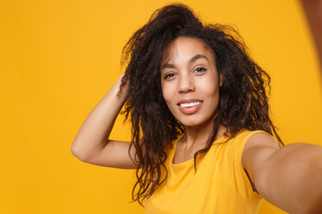 Close up of beautiful young african american woman girl in casual t-shirt posing isolated on yellow orange background. People lifestyle concept. Mock up copy space. Doing selfie shot on mobile phone.