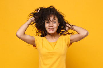 Fototapeta premium Smiling young african american woman girl in casual t-shirt posing isolated on yellow orange background studio portrait. People lifestyle concept. Mock up copy space. Having fun putting hands on head.