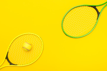 Top view of tennis rackets and ball on yellow background.