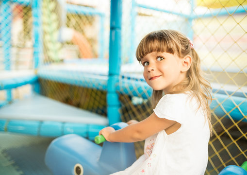 Little adorable girl play on toy horse on a playground near the sea on a sunny warm summer day during vacation. The concept of children's games on the street