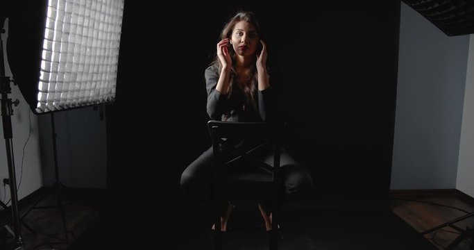 Young brunette in black suit sitting on chair in photo studio and posing to camera, fashion