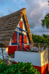 Small rural house with a triangular thatched roof. The red door and small windows with shutters. Santana city in Madeira island,Portugal