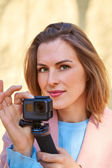 Portrait of beautiful blonde young woman with Action Camera making video. 