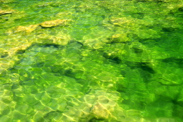 Yellow stones lie in the clear clear green water in the mountain river Krka in Croatia. Natural water background in lake or river, ecology