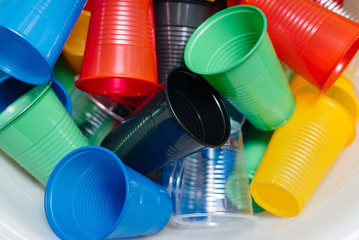 A large pile of multicolored plastic cups scattered on the floor. Pollution of the environment by human waste