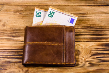 Brown leather wallet with fifty euro banknotes on the wooden background. Top view