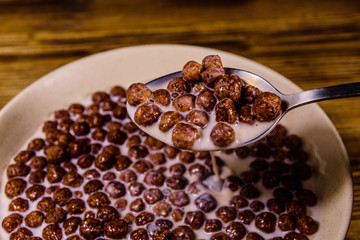 Ceramic plate with chocolate cereal balls in milk on wooden table