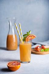 sweet freshly squeezed  orange juice with a slice of red orange and mint on a gray-blue background