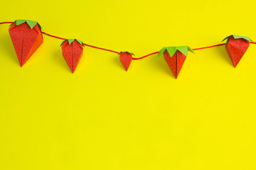paper strawberries joined by a red thread on a yellow background