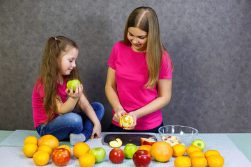 daughter and mom cut a fruit salad consisting of apple orange and mandarin