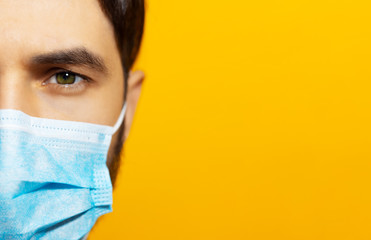 Close-up portrait of male face, wearing medical flu mask on background of orange color with copy...