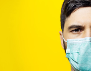 Close-up portrait of male face, wearing medical flu mask on background of yellow color with copy space.