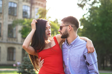 Obraz premium Beautiful couple of man and woman sitting on a bench in a park. Romantic theme with a girl and a guy. Spring Summer theme relationship, love, Valentine's day