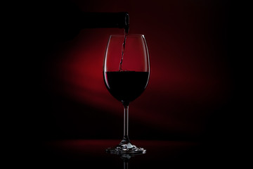 Red wine pouring in a glass from a bottle. Studio shot on black background.