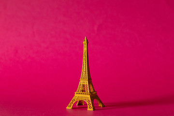 Fototapeta na wymiar Miniature yellow Eiffel Tower on pink background, Paris souvenir. Tourism and travel concept, space for copy. 