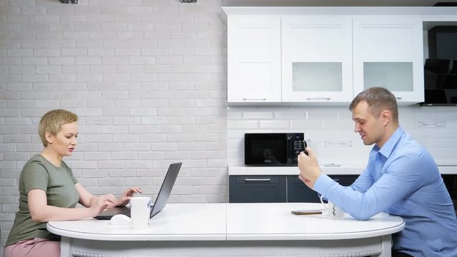 the modern housewife and the businessman sit at the kitchen, ignoring each other