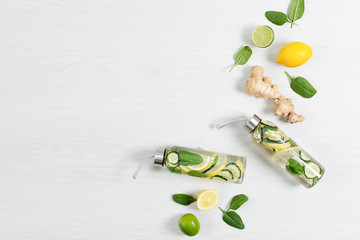 Detox infused water with lemon, lime, ginger and cucumber in a glass sport bottle on white wooden...