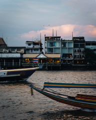 Boat crossing in front of residential buildings and restaurants at sunset in Bangkok