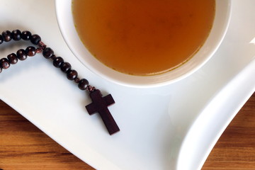 Christentum, Fastenzeit vor Ostern, ein Rosenkranz mit Kreuz neben einer Suppensch&uuml;ssel mit Br&uuml;he