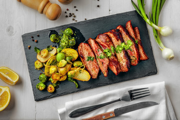 Medium rare meat hanger steak with brussels sprouts, potatoes and onion with herb sauce on a white wooden table. Delicious healthy food. Top view above.