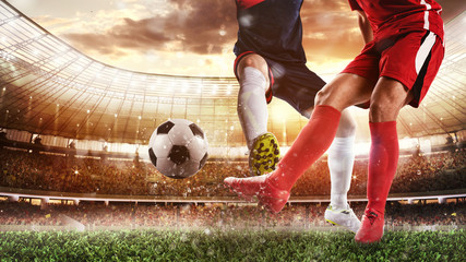 Soccer scene at the stadium with player in a red uniform kicking the ball and opponent in tackle to...