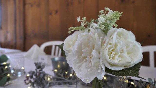 Wedding table setting with White garden roses and golden led lights. Wooden wall in the background. Close up parallax shot