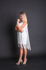 Girl with a microphone in a white dress in a photo studio on a black background