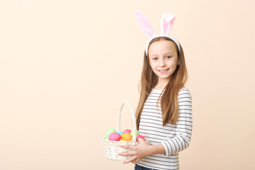 Obraz na płótnie Canvas Portrait of a little cute smiling girl with bunny ears and an Easter basket in hands on a colored background. Easter background with place to insert text.