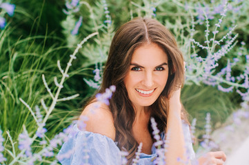 Outdoor close up portrait of pretty young woman with dark hair posing in summer garden with purple flowers