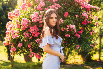 Fototapeta premium Outdoor portrait of pretty young woman posing in summer garden with pink roses