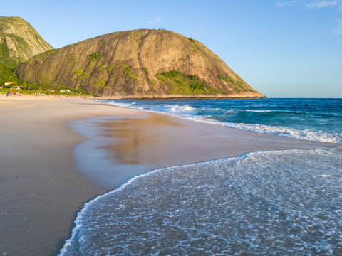 Spectacular day at the beach with naturally clean sands, clear waters, blue skies and few people. Waves arrive in the sand at Itacoatiara beach, Niteroi city, Rio de Janeiro State, Brazil.