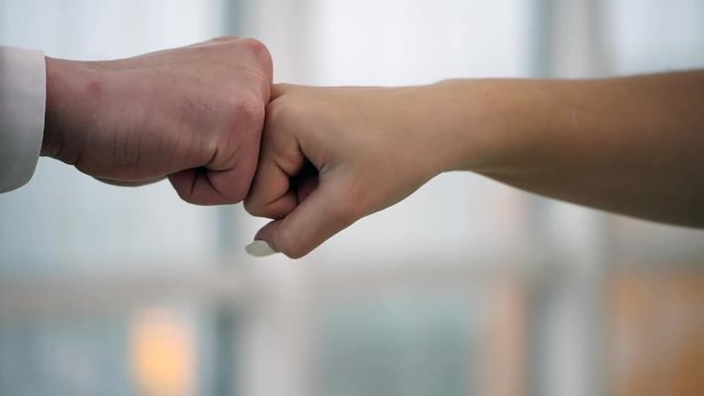 Fistbump of two business people. Friendly partners are firsbumping. Blurred background. Close up. Slow motion. Slowmo. 4K.
