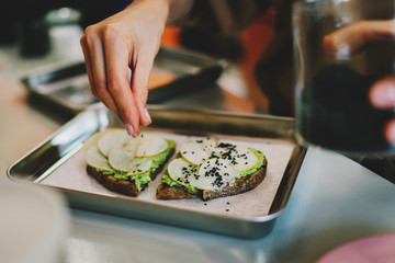 Close up photo of a female's hand adding spice to the open sandwich made of natural and healthy ingredients. Healthy food for the brunch. Sandwich with avocado for the breakfast. Gluten free food.